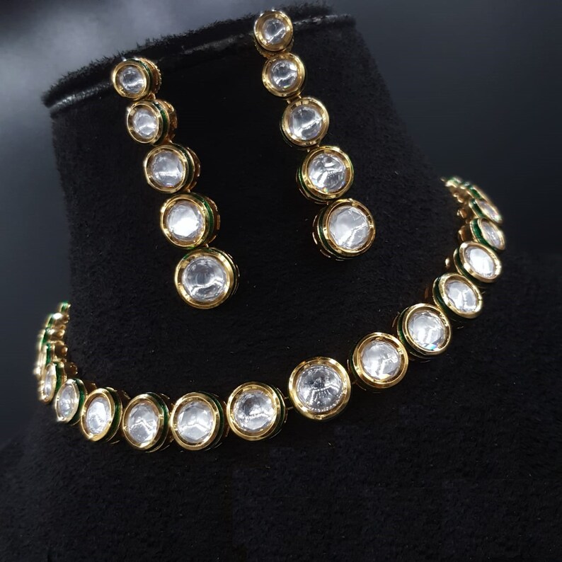 May include: A gold necklace and earrings set with a row of clear round stones with green accents.