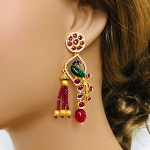 May include: Gold tone earrings with a peacock design, red and green enamel, and a red tassel. The earrings are adorned with red and clear stones.