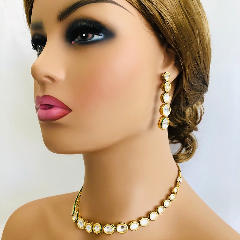 May include: A gold necklace and earrings set with clear round stones. The necklace is a choker style and the earrings are long and dangle.
