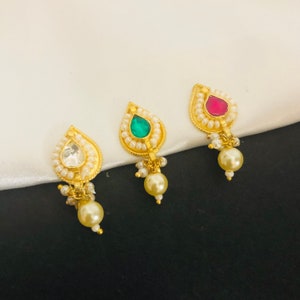 Puede incluir: Tres anillos de nariz de oro con detalles de perlas. Los anillos de nariz tienen forma de lágrima y presentan una piedra preciosa verde, roja y transparente en el centro.
