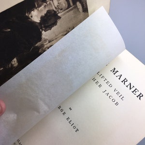May include: A vintage book titled "Lifted Veil" by R.G.E. Elliot. The book is open to a page with the title "The Marner" and the text "Lifted Veil" and "Her Jacob".