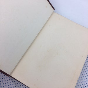 K&ouml;nnte beinhalten: Ein ge&ouml;ffnetes Buch mit braunem Einband und wei&szlig;en Seiten. Das Buch liegt auf einem blau-wei&szlig; gepunkteten Stoff.