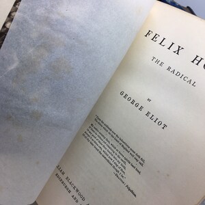 May include: A vintage book cover with the title "Felix Holt, The Radical" by George Eliot. The cover is cream-colored with black text and a quote from the book.