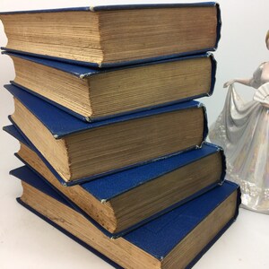 May include: A stack of five vintage hardcover books with blue spines and brown covers. The books are arranged in a pyramid shape.