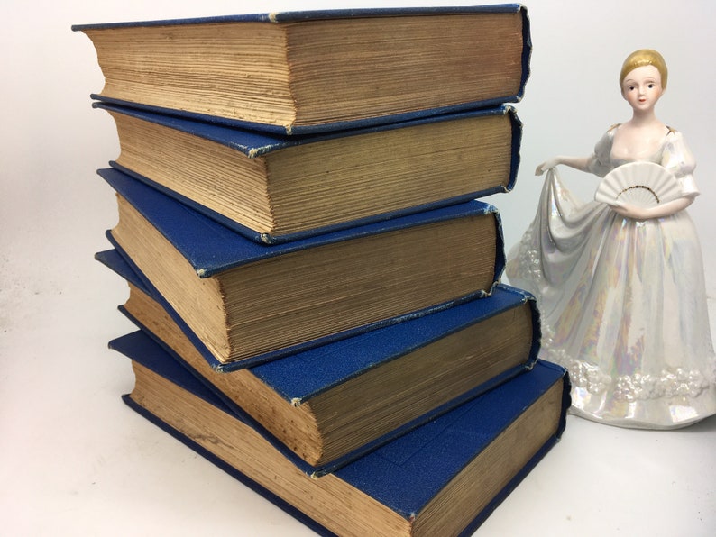 May include: A stack of five vintage hardcover books with blue spines and brown covers. The books are arranged in a pyramid shape.