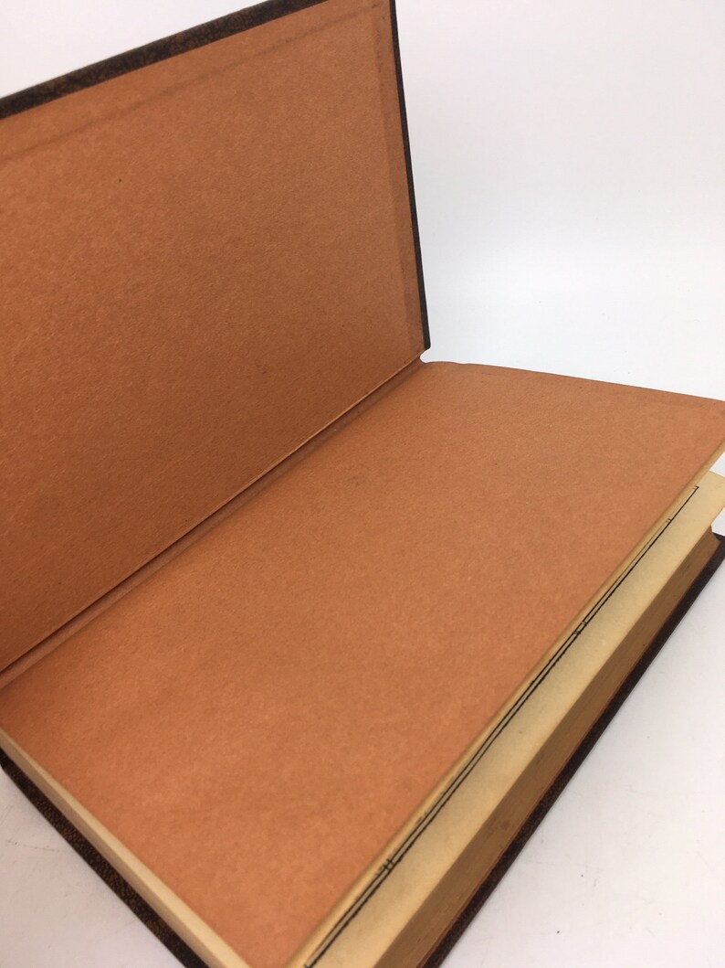 以下が含まれることがあります： 茶色の革の表紙とベージュの内部を持つ開いた本。ページは空白です。