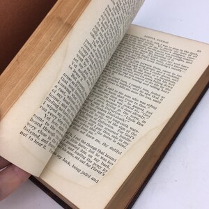 以下が含まれることがあります： 茶色の革張りで開かれた本のクローズアップ。ページは経年劣化で黄色く、テキストは黒いインクで印刷されています。本は「ローナ・ドゥーン」というタイトルで、ページのテキストは縛られて死んだまま放置された男性について説明しています。