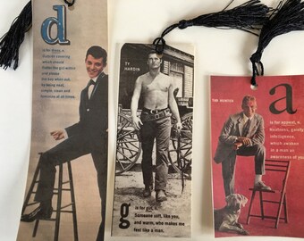 May include: Three bookmarks with different letters and images. The first bookmark has a blue letter "d" and a man in a suit. The second bookmark has a green letter "g" and a man with a bare chest. The third bookmark has a red letter "a" and a man in a suit sitting on a chair with a dog.