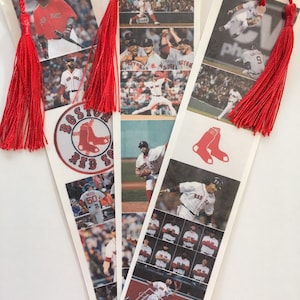 May include: Three red and white Boston Red Sox baseball team bookmarks with red tassels. The bookmarks feature images of players in action, including a player hitting a home run, a player at bat, and a player running the bases. The bookmarks also feature the Boston Red Sox logo and the team's name.