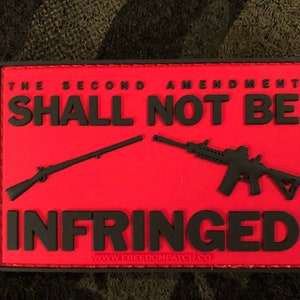 Könnte beinhalten: Roter Patch mit schwarzem Text und Bildern von zwei Waffen. Der Text lautet "The Second Amendment Shall Not Be Infringed" und "www.freedompatch.co".