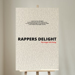 May include: Poster with the text "Rappers Delight" and "The Sugar Hill Gang" on a wooden easel. The background is a white wall. The text is in black and white.