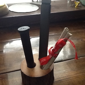 May include: A wooden pencil holder with three slots. Two black pens are in the slots and a bundle of white sticks with a red ribbon is in the third slot.