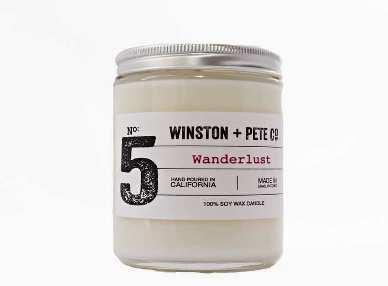 May include: A soy wax candle in a clear glass jar with a silver lid. The label reads "WINSTON + PETE CO" and "Wanderlust". The number "5" is prominently displayed. The candle is hand-poured in California.