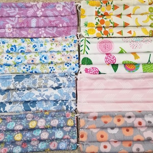 Może przedstawiać: Zestaw dziesięciu masek na twarz z różnych materiałów. Maski mają wzory kwiatowe, geometryczne i owocowe w kolorze różowym, niebieskim, białym i szarym.