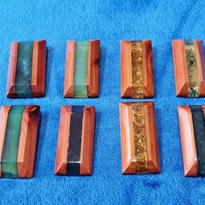 May include: Eight rectangular wooden coasters with a clear resin inlay. The resin inlays feature different colors and patterns, including green, black, gold glitter, and a green and black swirl.