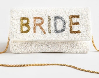 May include: White beaded clutch with a gold chain strap. The clutch has the word "BRIDE" spelled out in colorful beads.