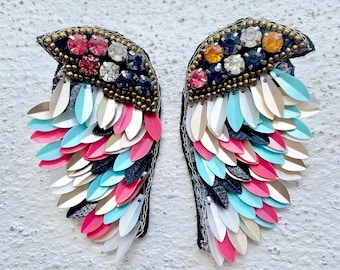 May include: A pair of colorful wings made of sequins and beads. The wings are black, white, pink, blue, and gold. They are a decorative item that could be used for a costume or a craft project.