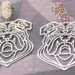 May include: A pair of gold-tone bulldog earrings. The earrings are made of metal and feature a detailed outline of a bulldog's face.