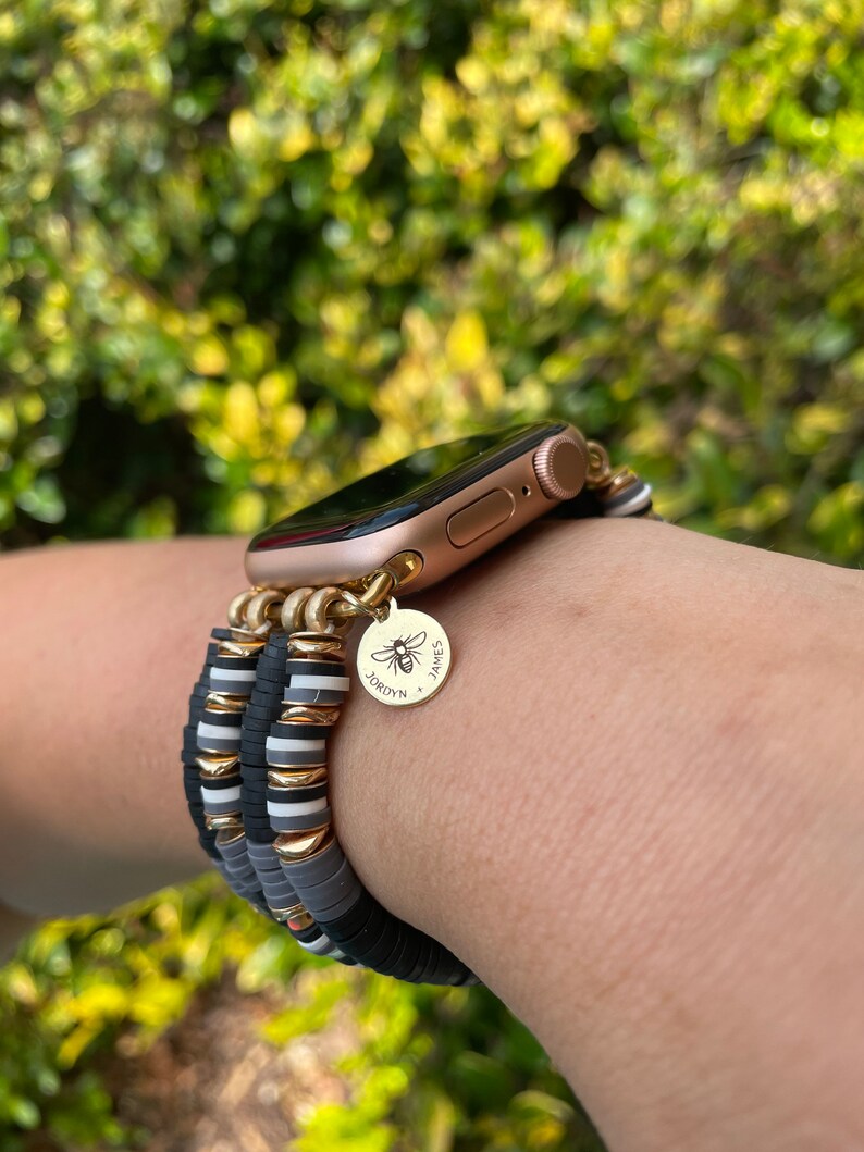May include: A gold Apple Watch with a black and white beaded bracelet. The bracelet has a gold charm with a bee and the names "Jordyn" and "James".