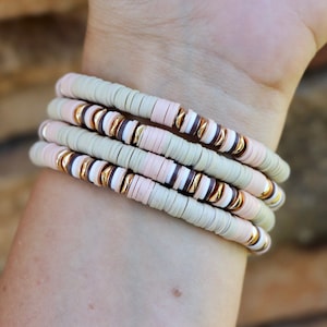 May include: A set of four bracelets with beige, pink, and brown ceramic beads and gold accents.
