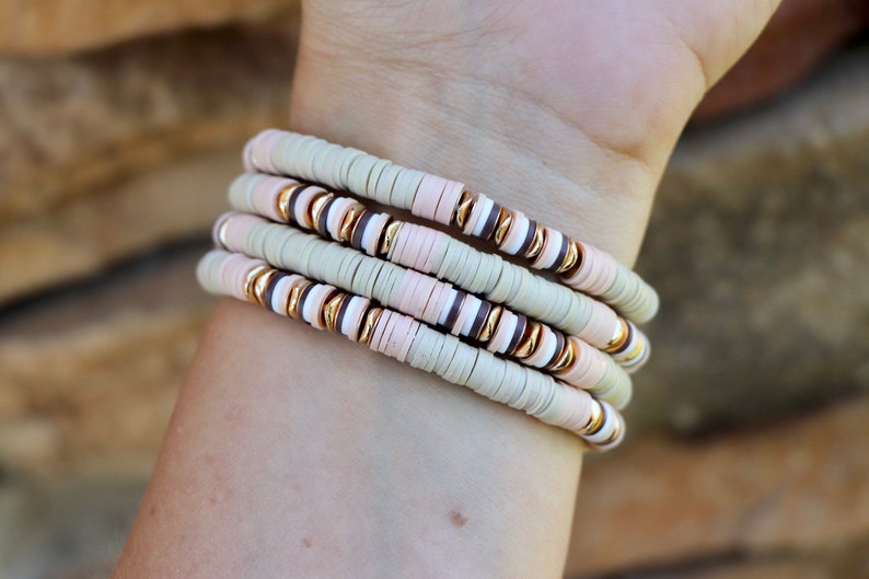 May include: A set of four bracelets with beige, pink, and brown ceramic beads and gold accents.