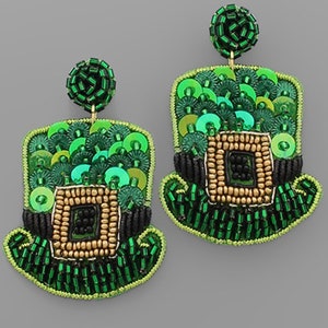 以下が含まれることがあります： 緑と金のビーズでできた、レプリコーンの帽子型のイヤリングのペア。帽子には黒いビーズのバンドと金のバックルが付いています。