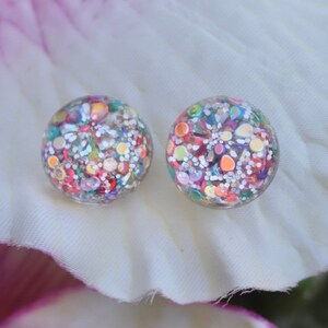 May include: A pair of clear glass earrings with colorful confetti and glitter inside. The earrings are round and have a smooth, polished finish.