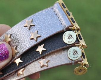 May include: Three gold-toned Apple Watch bands with star-shaped studs. The bands are layered on top of each other, with the top band being silver, the middle band being black, and the bottom band being gold. Each band has a gold charm attached to it with the text "JORDYN x JAMES".