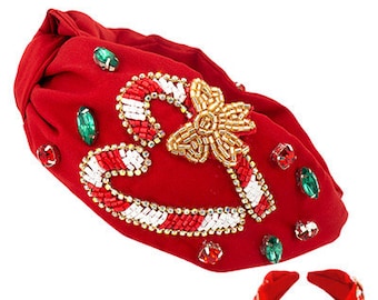 Op de afbeelding: Rode stoffen haarband met een zuurstokontwerp gemaakt van witte en rode kralen, en een gouden strik. De haarband is versierd met groene en rode edelstenen. Een kleinere bijpassende haarband is ook afgebeeld.