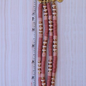 May include: A pink and white beaded Apple Watch band with gold accents. The band is made of three rows of beads and has a gold clasp.
