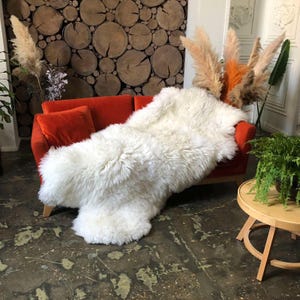 May include: A white sheepskin rug draped over an orange sofa. The rug is fluffy and soft, and the sofa is a modern design with a low back and wide arms.