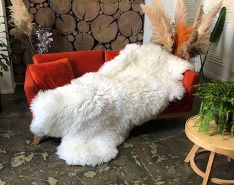 May include: A white sheepskin rug draped over an orange sofa. The rug is fluffy and soft, and the sofa is a modern design with a low back and wide arms.