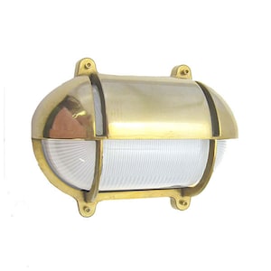 May include: A brass outdoor wall light fixture with a clear, ribbed glass lens. The light is oval shaped and has a traditional design.