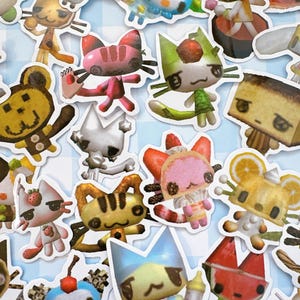 May include: A collection of colorful cat-like character stickers with various food-themed designs, including strawberries, watermelon, and oranges. The stickers are on a light blue and white checkered background.