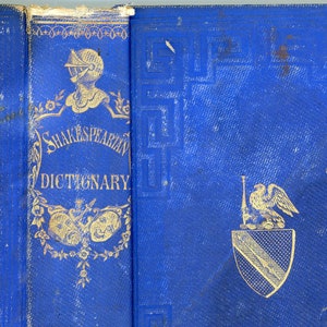 Könnte beinhalten: Ein blaues Buch mit goldener Beschriftung, die "Shakespearean Dictionary" lautet. Der Einband zeigt eine goldene Illustration eines Ritters in Rüstung, zwei Masken und ein Wappen.