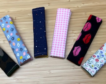 May include: Six fabric strips with different patterns, including camouflage, floral, polka dots, gingham, lips, and stars. The strips are all approximately the same size and are arranged in a semi-circle on a wooden surface.