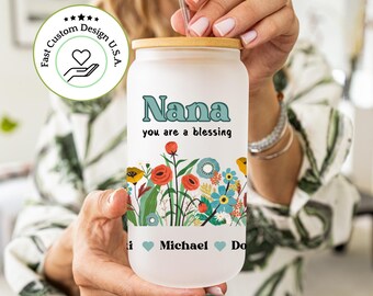May include: White frosted tumbler with a bamboo lid and a straw. The tumbler has a floral design with red, blue, and green flowers. The text "Nana you are a blessing" is printed on the tumbler. The text "Michael" is printed on the bottom of the tumbler.