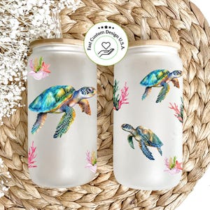 May include: Two clear glass tumblers with a bamboo lid and a reusable straw. The tumblers feature a white background with a repeating pattern of sea turtles and coral. The text "Fast Custom Design U.S.A." is printed on the tumblers.