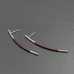 May include: A pair of silver and brown curved earrings. The earrings are made of a thin metal wire with a brown material wrapped around it.