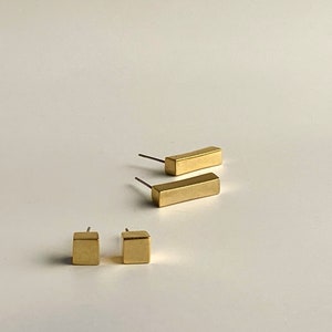May include: A set of three gold-toned earrings. Two earrings are rectangular in shape and one earring is square.