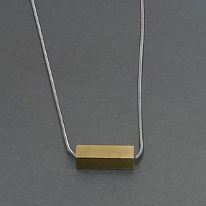 May include: A silver chain necklace with a gold rectangular pendant.