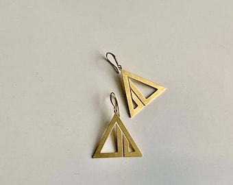 May include: A pair of gold-toned triangle earrings with a geometric design. The earrings are made of two triangles, one inside the other.
