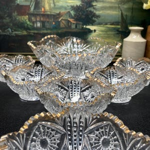 May include: Set of six clear glass bowls with gold trim. The bowls are all different sizes and shapes, and they are arranged in a circle on a black surface.