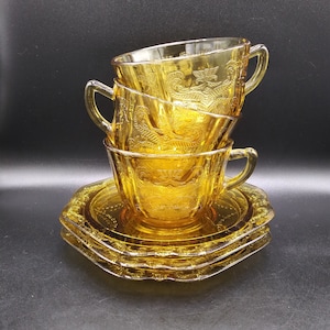 May include: A set of three amber glass teacups and saucers with a floral pattern. The cups are stacked on top of each other and the saucers are underneath.