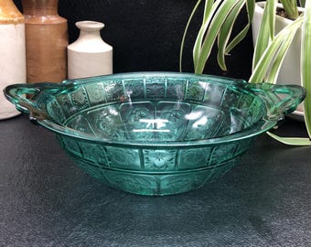 May include: A green glass bowl with two handles. The bowl has a decorative pattern and is perfect for serving salads or desserts.
