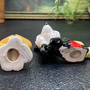 May include: Three ceramic figurines of Mickey Mouse characters. The figurines are painted in yellow, black, white, and red. The bottom of each figurine has a copyright notice that reads "Walt Disney Productions, Japan".