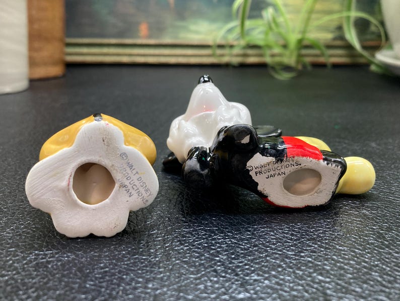May include: Three ceramic figurines of Mickey Mouse characters. The figurines are painted in yellow, black, white, and red. The bottom of each figurine has a copyright notice that reads "Walt Disney Productions, Japan".
