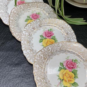 May include: Set of five white porcelain dessert plates with a gold rim and floral design. Each plate features a pink and yellow rose with green leaves.