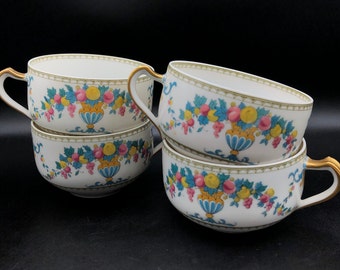 May include: Four white ceramic teacups with gold trim and a floral pattern featuring pink, yellow, and blue fruit and leaves.