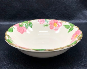 May include: A white ceramic bowl with a floral design. The bowl has a scalloped edge and is decorated with pink roses and green leaves. The bowl has a gold trim around the edge.